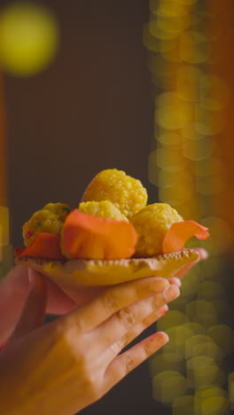 Vertical-Video-Close-Up-Of-Man-Handing-Dish-Of-Ladoo-To-Woman-Celebrating-Festival-Of-Diwali